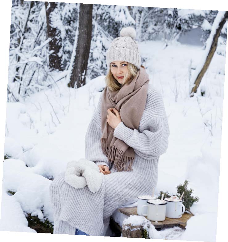 Kvinna klädd i vita vinterkläder sitter på stock i en snöklädd skog. Bredvid sig har hon en kaffebricka.