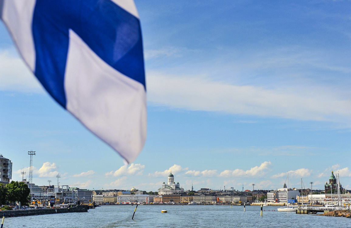 vy över vatten med staden i bakrunden och en flik av finska flaggan i förgrunden.