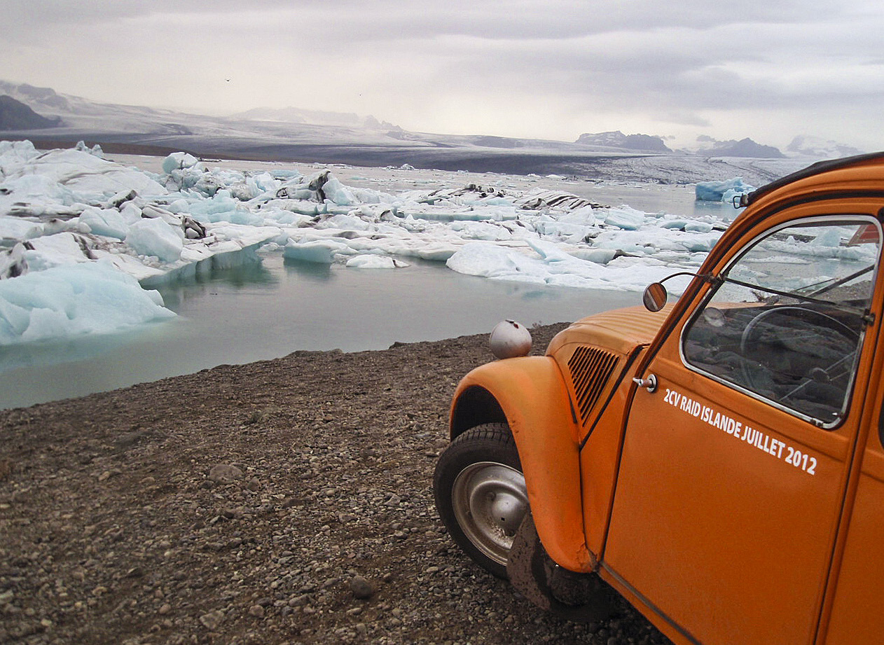 i förgrunden framändan av en orange citroën CV2, framför bilen breder en glaciär ut sig.